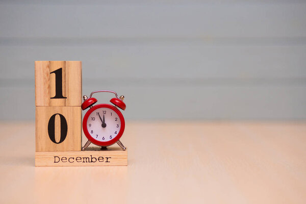 December 10th set on wooden calendar and red alarm clock with blue background. Clock showing five minutes to midnight