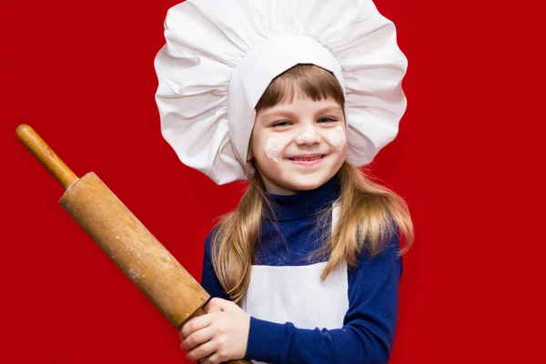 シェフの制服を着た幸せな少女は 赤に分離された麺棒を保持しています 子供のシェフ 料理のコンセプト — ストック写真