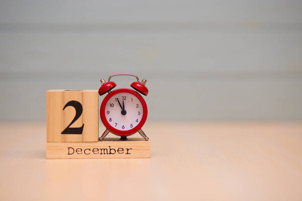 December 2nd set on wooden calendar and red alarm clock with blue background. Clock showing five minutes to midnight