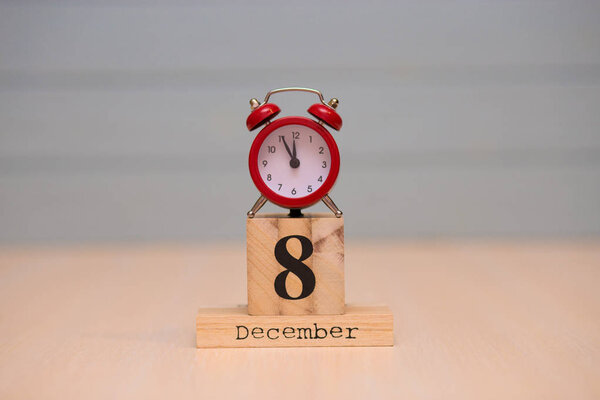 December 8th set on wooden calendar and red alarm clock with blue background. Clock showing five minutes to midnight