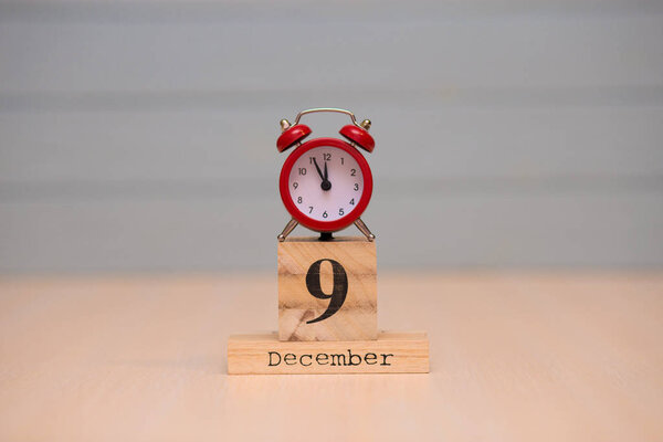 December 9th set on wooden calendar and red alarm clock with blue background. Clock showing five minutes to midnight