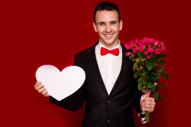 Çiçekler ve kırmızı zemin üzerine izole büyük kağıt kalp ile genç gülmek işadamı portresi