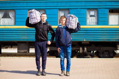 Tren istasyonunda büyük çanta ile iki adam. Tren