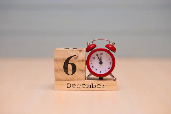 December 6th set on wooden calendar and red alarm clock with blue background. Clock showing five minutes to midnight