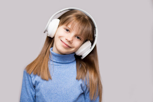 Счастливый улыбчивый ребенок наслаждается музыкой в наушниках на белом фоне
