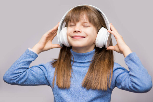 Energy kid girl with headphones listening to music with closed eyes on white background in studio.