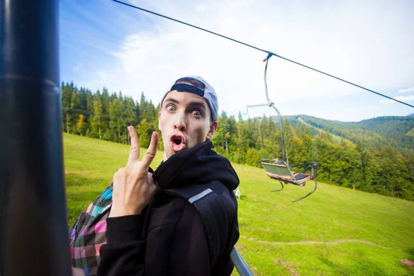 man with funny face sitting on the chairlift during summer hike in mountains