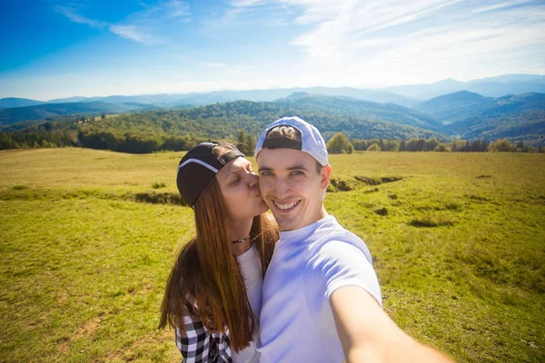 Young couple hiking taking selfie with smart phone. Happy young man and woman taking self portrait with mountain scenery background