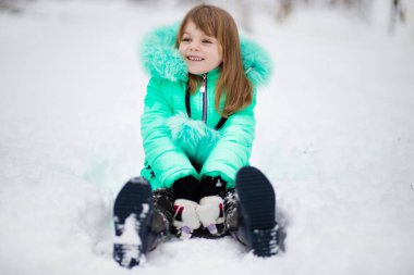 Komik küçük kız kar yağarken güzel kış parkında eğleniyor.