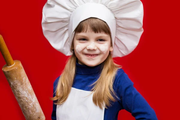 シェフの制服を着た幸せな少女は 赤に分離された麺棒を保持しています 子供のシェフ 調理プロセスの概念 — ストック写真