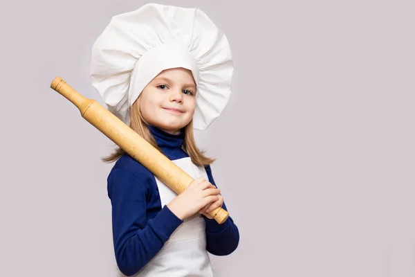 Children cook. Happy little girl in chef uniform holds rolling pin isolated on white background. Kid chef.