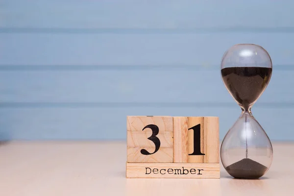 December 31st set on wooden calendar and hourglass with blue background. Calendar date of Financial Year end