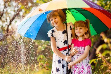 Renkli şemsiye sonbahar duş yağmur altında oynayan çocuklarla. Küçük kızlar yağmurlu hava ile parkta oynamak. Sonbahar açık eğlenceli çocuklar için.