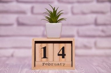 14 Şubat. Beyaz tuğla zemin üzerine yeşil çiçekli ahşap takviminde ayın gün 14. Mutlu sevgililer günü.