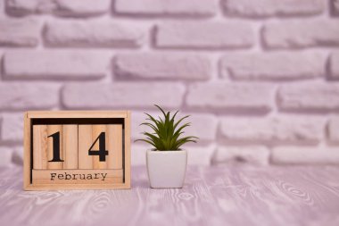 14 Şubat. Beyaz tuğla zemin üzerine yeşil çiçekli ahşap takviminde ayın gün 14. Mutlu sevgililer günü.