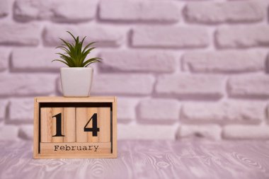 14 Şubat. Beyaz tuğla zemin üzerine yeşil çiçekli ahşap takviminde ayın gün 14. Mutlu sevgililer günü.