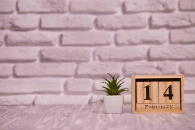 14 Şubat. Beyaz tuğla zemin üzerine yeşil çiçekli ahşap takviminde ayın gün 14. Mutlu sevgililer günü.