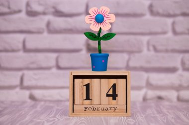 14 Şubat. Oyuncak çiçek beyaz tuğla zemin üzerine ahşap takviminde ayın gün 14. Mutlu sevgililer günü.