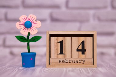 14 Şubat. Oyuncak çiçek beyaz tuğla zemin üzerine ahşap takviminde ayın gün 14. Mutlu sevgililer günü.