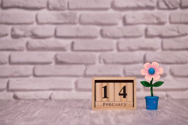 14 Şubat. Oyuncak çiçek beyaz tuğla zemin üzerine ahşap takviminde ayın gün 14. Mutlu sevgililer günü.