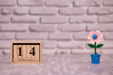 14 Şubat. Oyuncak çiçek beyaz tuğla zemin üzerine ahşap takviminde ayın gün 14. Mutlu sevgililer günü.