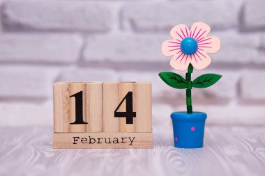 14 Şubat. Oyuncak çiçek beyaz tuğla zemin üzerine ahşap takviminde ayın gün 14. Mutlu sevgililer günü.
