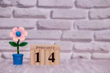 14 Şubat. Oyuncak çiçek beyaz tuğla zemin üzerine ahşap takviminde ayın gün 14. Mutlu sevgililer günü.