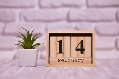 14 Şubat. Beyaz tuğla zemin üzerine yeşil çiçekli ahşap takviminde ayın gün 14. Mutlu sevgililer günü.