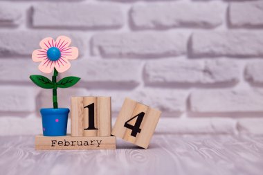 14 Şubat. Oyuncak çiçek beyaz tuğla zemin üzerine ahşap takviminde ayın gün 14. Mutlu sevgililer günü.