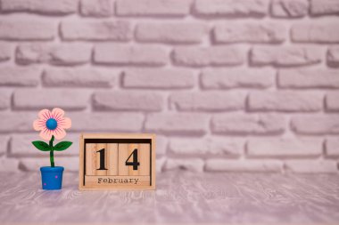 14 Şubat. Oyuncak çiçek beyaz tuğla zemin üzerine ahşap takviminde ayın gün 14. Mutlu sevgililer günü.