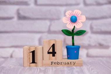 14 Şubat. Oyuncak çiçek beyaz tuğla zemin üzerine ahşap takviminde ayın gün 14. Mutlu sevgililer günü.