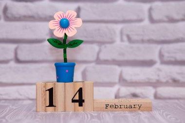 14 Şubat. Oyuncak çiçek beyaz tuğla zemin üzerine ahşap takviminde ayın gün 14. Mutlu sevgililer günü.