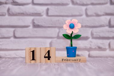 14 Şubat. Oyuncak çiçek beyaz tuğla zemin üzerine ahşap takviminde ayın gün 14. Mutlu sevgililer günü.