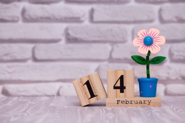 14 Şubat. Oyuncak çiçek beyaz tuğla zemin üzerine ahşap takviminde ayın gün 14. Mutlu sevgililer günü.
