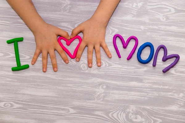 J'adore maman texte de plasticine avec des mains d'enfant sur fond blanc en bois. Joyeuse fête des mères. Fun enfants artisanat artisanal — Photo