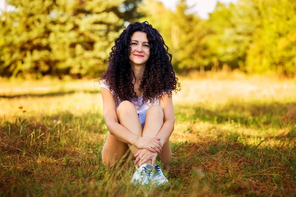 Mooie gekrulde vrouw poseren op gras in zonnige dag — Stockfoto