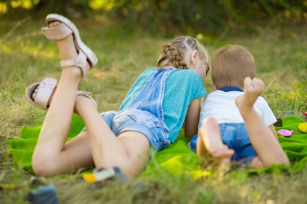 Los niños se acuestan en la hierba de verano y ven dibujos animados en el teléfono. Jugar juegos en el teléfono inteligente. Estilo de vida moderno y concepto de niños . —  Fotos de Stock