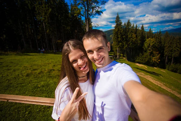Young couple hiking taking selfie with smart phone. Happy young man and woman taking self portrait with mountain scenery