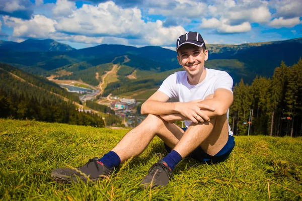 Человек турист расслабляясь на вершине холма и любуясь красивым видом на горную долину летом — стоковое фото