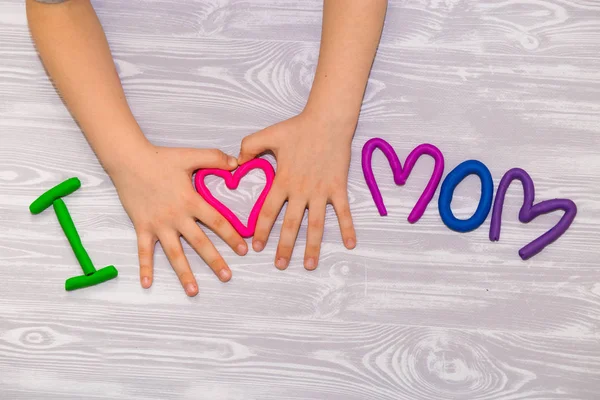 I love mom text from plasticine with kid hands on white wooden background. Happy mothers day. Fun kids handmade craft — Stock Photo, Image
