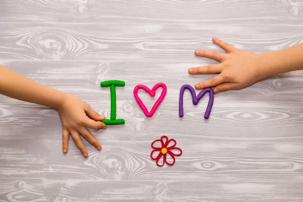 I love mom text from plasticine with kid hands on white wooden background. Happy mothers day. Fun kids handmade craft