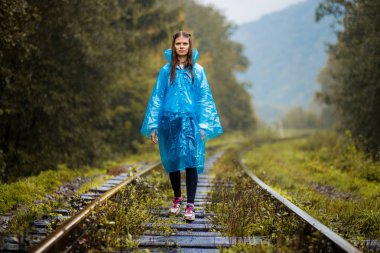 Kız Gezgin giyiyor mavi ceket ve go orman tren tarafından. Mavi yağmur ceket kız ormanda, sis yürür iken koyu yeşil tonları ile sonbahar, yağmur sezonu