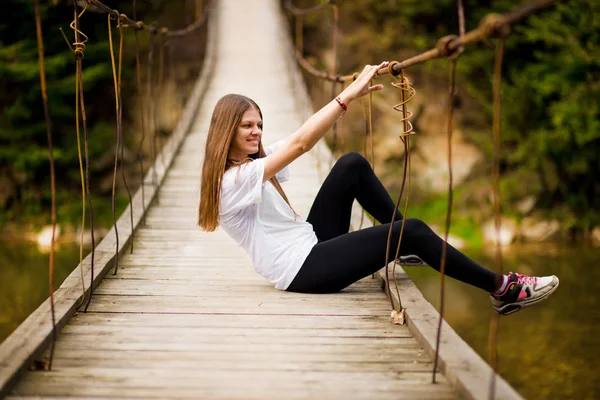 Toeristische vrouw lopen door lange houten hangbrug boven rivier. — Stockfoto