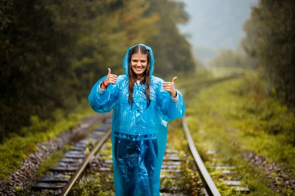 Chica viajera vistiendo chaqueta azul e ir por ferrocarril forestal. Otoño y temporada de lluvias con tonos verde oscuro, mientras que la niña con chaqueta de lluvia azul camina en el bosque, niebla, lluvia y nubes —  Fotos de Stock