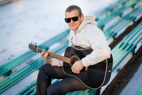 Joven sentado en los escalones tocando la guitarra y cantando, concepto musical — Foto de Stock