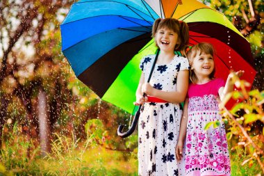 Renkli şemsiye sonbahar duş yağmur altında oynayan çocuklarla. Küçük kızlar Yağmurlu hava ile parkta oynamak. Sonbahar açık eğlenceli çocuklar için. Yağmur damlaları yakalamak çocuk.