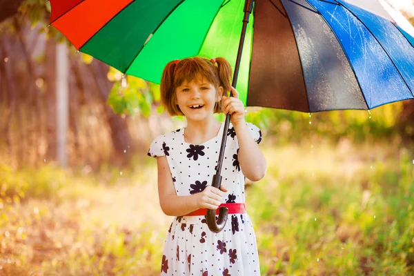 Happy child girl walk with multicolored umbrella under rain — Stock Photo, Image