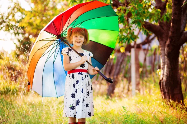 Щаслива дівчинка гуляє з різнокольоровою парасолькою під дощем — стокове фото
