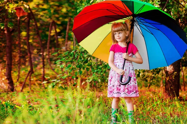 Щаслива дівчинка гуляє з різнокольоровою парасолькою під дощем — стокове фото