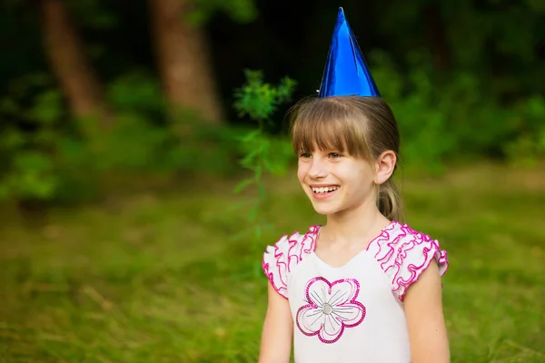 幸せな小さな女の子子かわいいとお祝いコーン キャップの美しい芝生の上に座って、楽しい時を過す — ストック写真